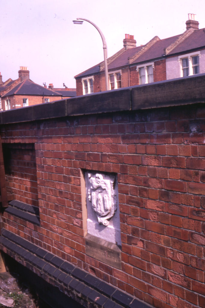 Merchant Taylors' Stone (1652), Roe Bridge, London SW16. In north parapet wall. Inscription says This bridge was made at the cost of the Worshipful Company of Merchant Taylors. Bridge re-built and stone reset several times since.