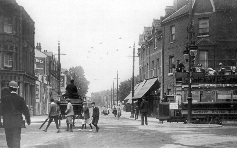 Postmarked 1907, the year in which Wimbledon saw its first trams, this view looks up Merton Road. A LUT tram is swinging round from Merton High Street. It advertises Skewes store in Wimbledon, as well as Sandown Park Races.